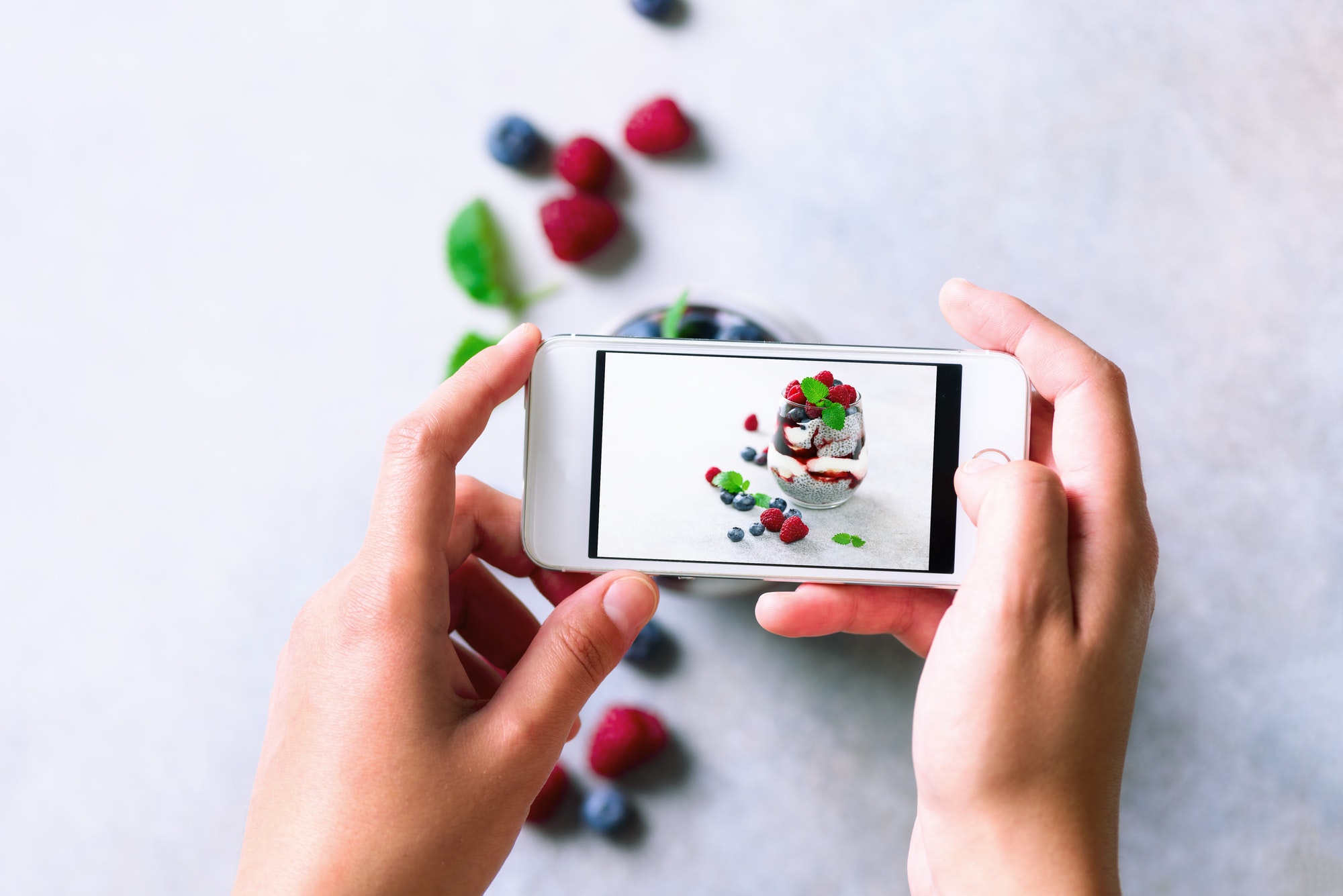 Girl is taking photos of breakfast, chia pudding with berries to mobile phone. Social media
