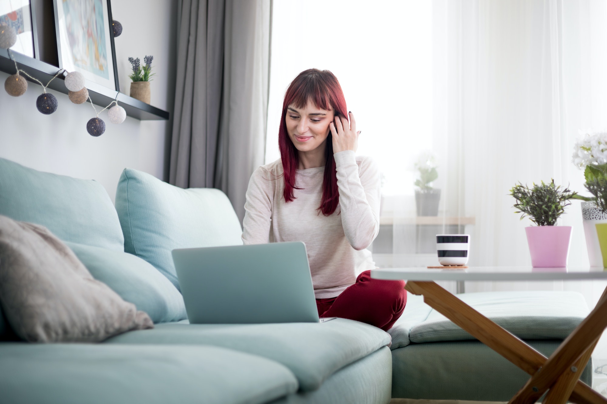 Cheerful woman browsing internet with laptop while sitting on sofa at home