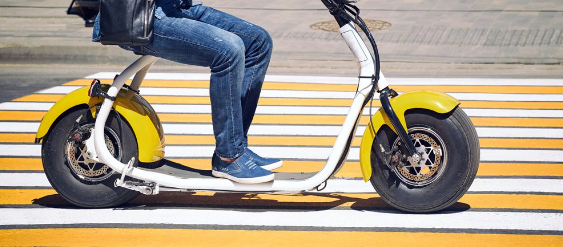 An electric motorcycle, scooter, or bicycle rides in the city on the road through a pedestrian crossing. The concept of ecology and traffic safety in the city.
