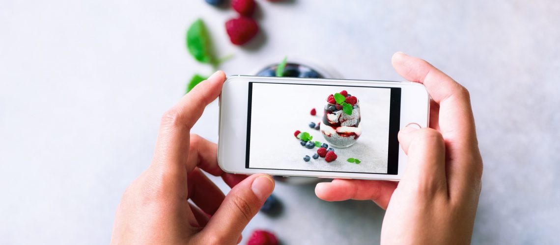 Girl is taking photos of breakfast, chia pudding with berries to mobile phone. Social media